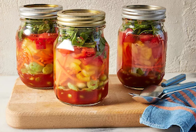 Three mason jars with vegetable soup ingredients sitting on a cutting board.