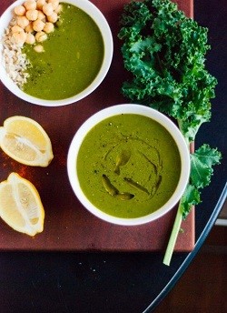 two bowls of vegan green soup with lemon wedges