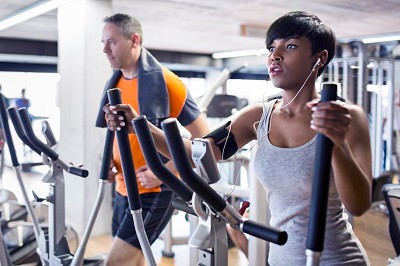 man and woman next to each other on elliptical machines in gym