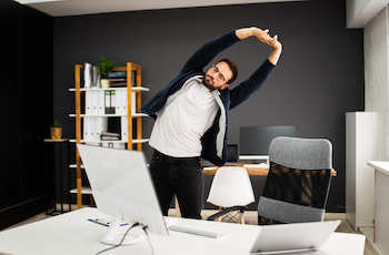 A man standing and stretching near his desk