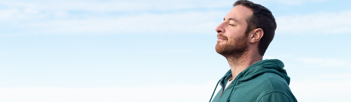 Man taking a deep breath with blue sky in the background