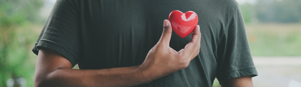 A man's chest and he's holding up a red heart next to it