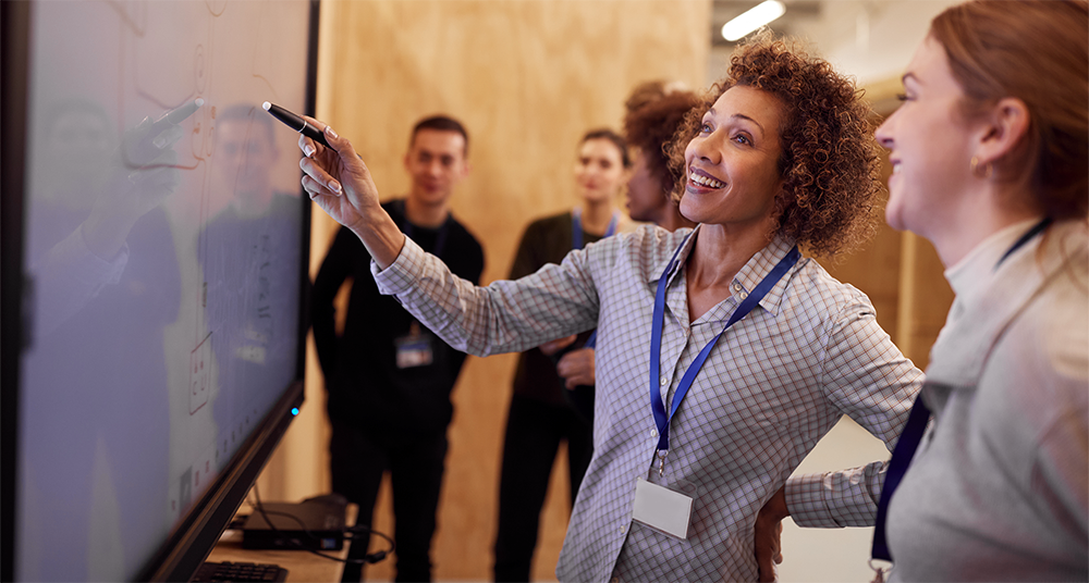 stock photo of woman pointing to large screen as several people watch