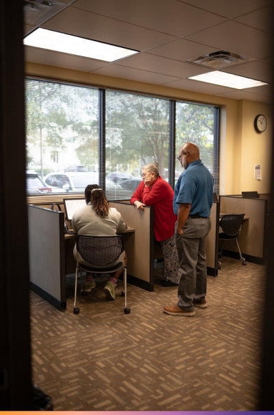 A woman sits at a computer while another woman and man look over her shoulders