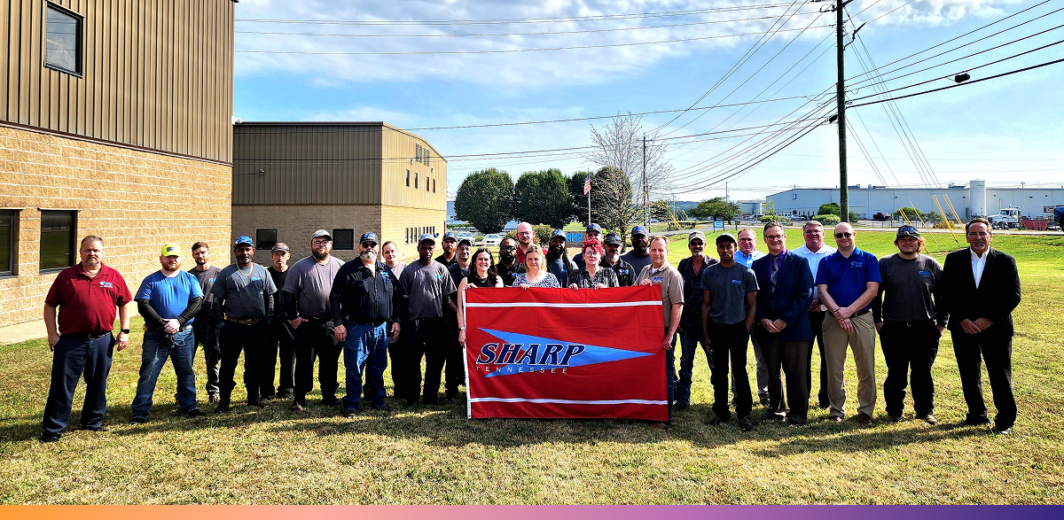 A large group of people stand with a SHARP flag