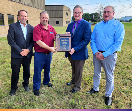Four men pose for a photo, with two holding a plaque