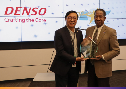 Two men hold a crystal award in front of the DENSO: Crafting the Core and Volunteer STAR logos