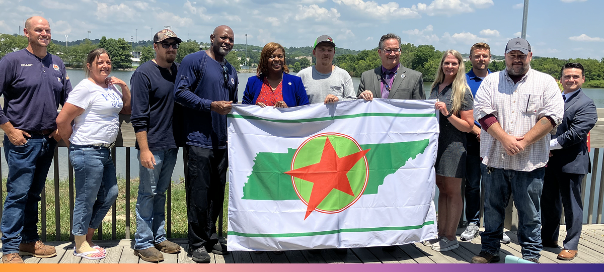 11 people pose for a photo, with five holding the Volunteer STAR flag