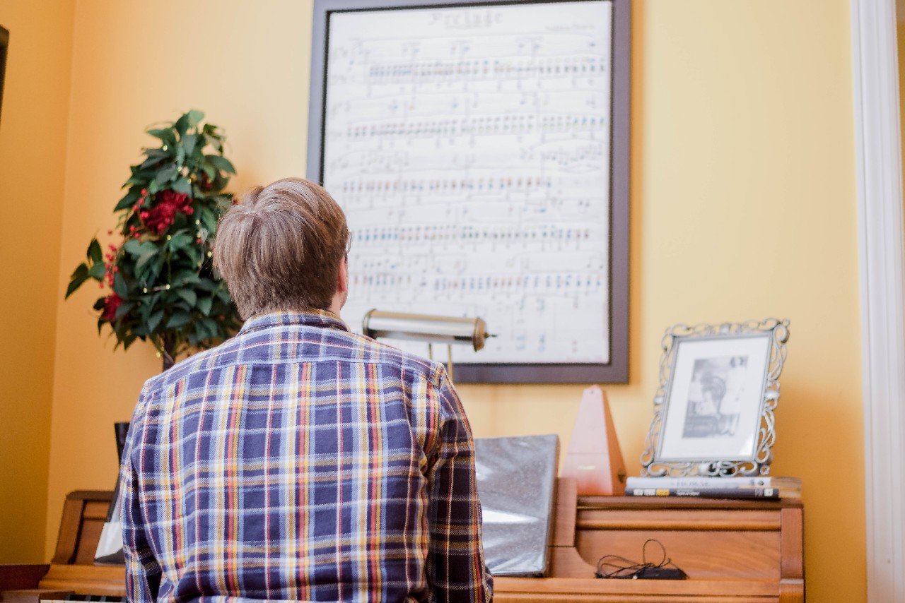 DSC_7813 Ben looks up at a painting of song chords painted as piano sheet music that hands above his antique piano