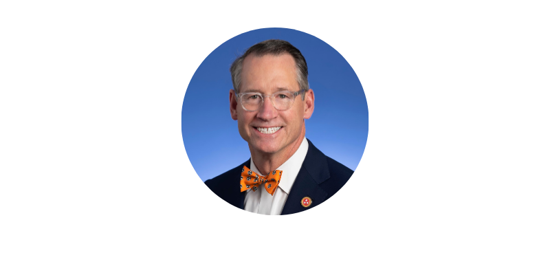 Aging Conference Headshots - Bo Watson Man with eyeglasses and orange bowtie smiling in front of blue background.