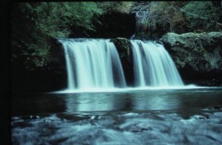 A double waterfall cascades over a ledge into a stream