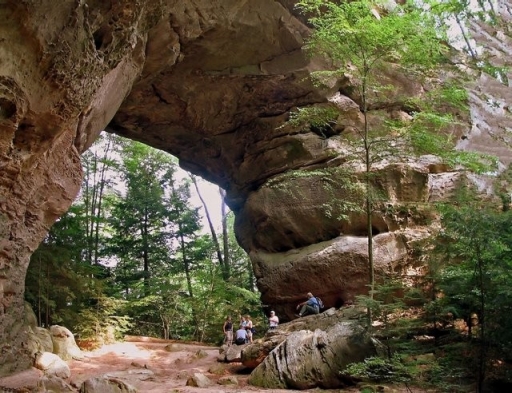 People hike under a large stone arch