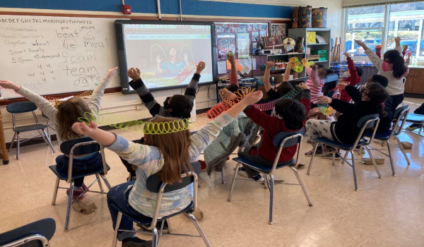 Childred learning through a virtual lesson Children in chairs in a classroom with toy coils
