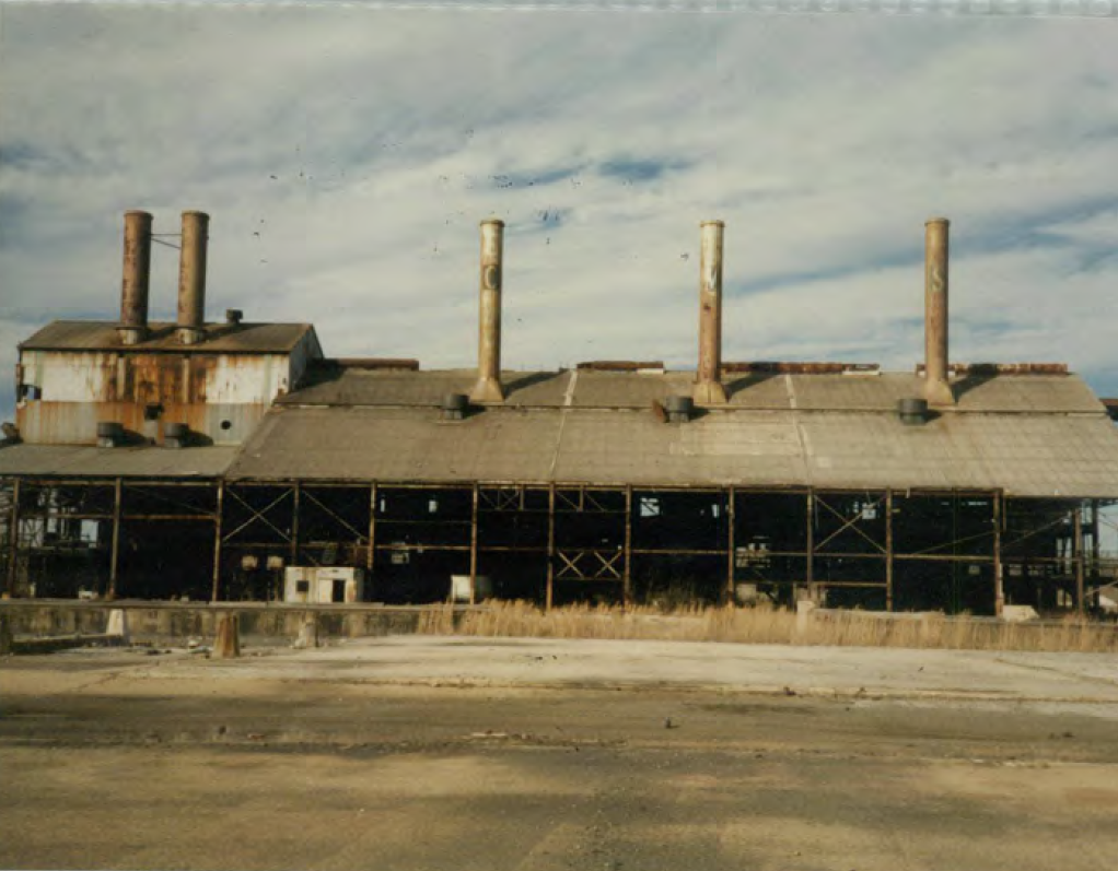Chromasco furnace building smokestacks The since-dempolished Chromasco facility furnace building featuring rusty roof and iron scaffolding below an ominous smokestack on a yellow-grassy concrete slab..