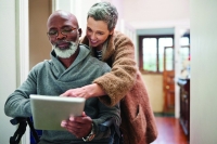 An elderly woman assists a man in a wheelchair using a tablet An elderly woman assists a man in a wheelchair using a tablet