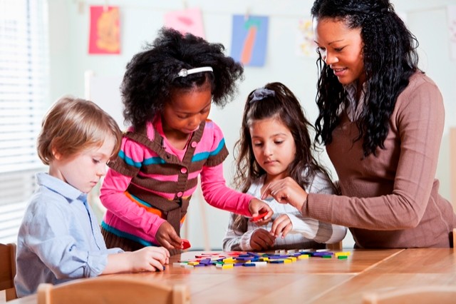 Multi-ethnic teacher (20s) and preschool children (4 years) in classroom working with colorful wooden shapes.