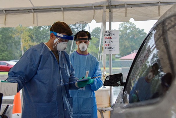Soldiers in protective gear speak with a civilian in a vehicle in order to test them for Covid-19
