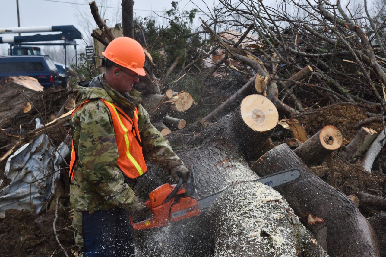 Tennessee Guard Clears Debris in Putnam County Tennessee Guard Soldier in uniform with orange construction hat using chainsaw to cut a tree into sections