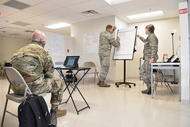 ) Staff Sgt. Brandon Hill, Maj. William Fitzwater and Lt. Col. Elizabeth Cooper work to establish COVID-19 sanitation procedures at Nashville’s Alternate Care Site, Aug. 27. 3 Military members in uniform work in an office on procedures
