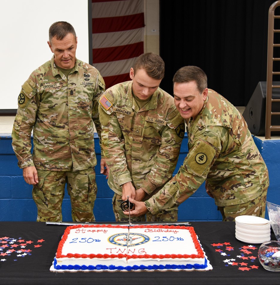 Tennessee’s Senior Enlisted Leader, Command Sgt. Maj. Dale Crockett, looks on as Pfc. Christian Amacher and Col. Mark Phillips perform the ceremonial cake cutting during the Tennessee National Guard’s 250th birthday celebration at Nashville’s Joint Force Headquarters on August 16. (photo by retired Sgt. 1st Class Edgar Castro) Tennessee’s Senior Enlisted Leader, Command Sgt. Maj. Dale Crockett, looks on as Pfc. Christian Amacher and Col. Mark Phillips perform the ceremonial cake cutting during the Tennessee National Guard’s 250th birthday celebration at Nashville’s Joint Force Headquarters on August 16. (photo by retired Sgt. 1st Class Edgar Castro)