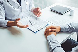 a top down view of a doctor sitting across a table from a person whose hands are folded