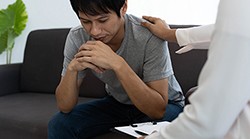 young man with head down, looking at the floor, being consoled by a person in a white coat