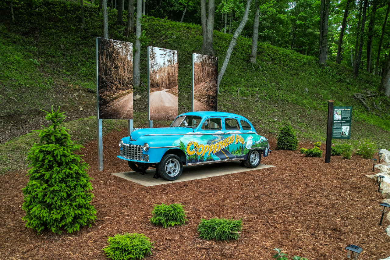 Copperhead Road Landmark A colorful vintage car display marks the Copperhead Road landmark along a wooded roadside.