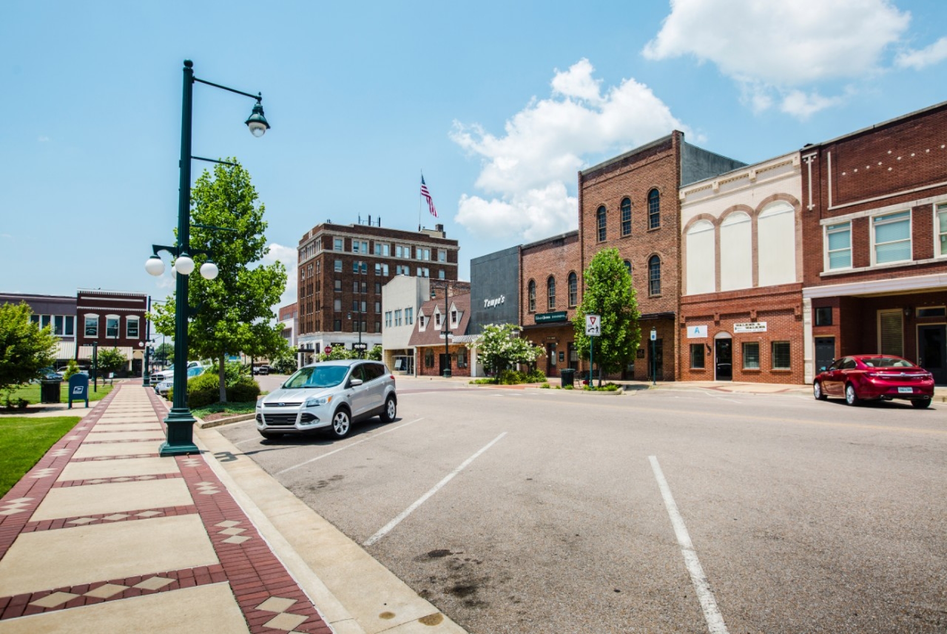 Dyersburg 1 Small-town main street with brick storefronts, parked cars, and decorative streetlights under a blue sky.