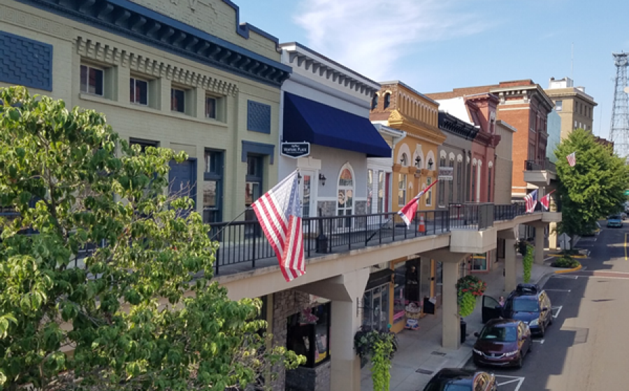 Colorful historic storefronts line a downtown street with balconies, flags, and parked cars.