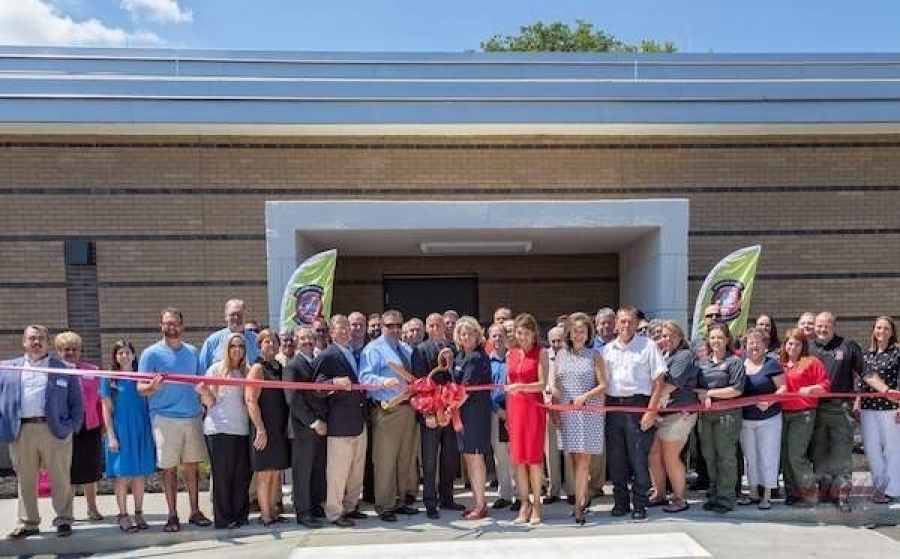 A large group of people gathers outside a public building for a ribbon-cutting ceremony.