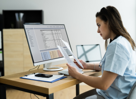 Woman sitting at computer looking over bills 