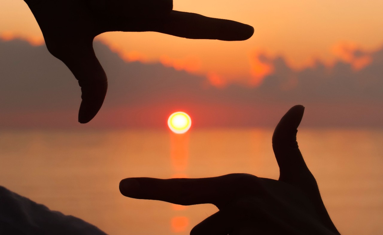 Index fingers and thumb framing sun going down
