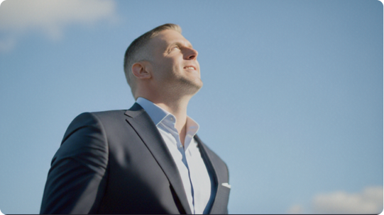 Photo of a man in a business suit looking up and smiling at a blue sky