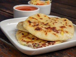 Pupusas Revueltas: Salvadoran-style Stuffed Masa Cakes pupusas revueltas on a dish with dipping sauces in the background