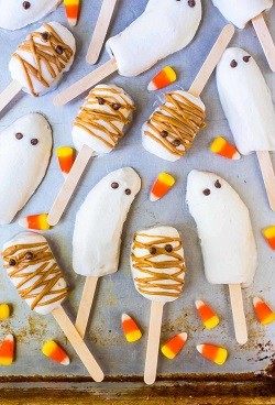 banana popsicles that look like ghost characters with candy corn scattered