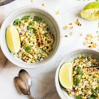 Mexican Elote two bowls of roasted corn in a bowl with lime wedges in the bowl