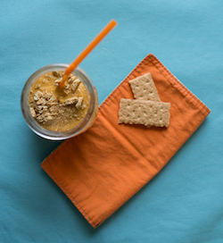 Pumpkin Pie Smoothie a pumpkin pie smoothie in a glass with an orange straw, an orange napkin on the counter and graham crackers on top of the napkin