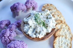 dill pickle dip in a small bowl surrounded with crackers and cauliflower