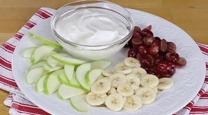 Honey Vanilla Yogurt Dip dip on a plate with grapes and slices of apples and banana