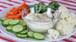 dip in a bowl with broccoli, cucumber, cauliflower and carrots on a plate
