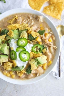 a bowl of white chicken chili topped with jalapeno peppers, avocado and tortilla chips