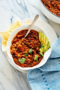 a bowl of vegetarian chili topped with avocado and a side of tortilla chips
