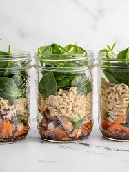 three majon jars with chicken, noodles and veggies in it