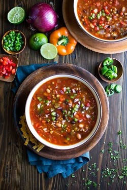 Vegetarian Taco Soup two bowls of vegetarian taco soup with assorted ingredients around the counter, including red onion, bell pepper and lime