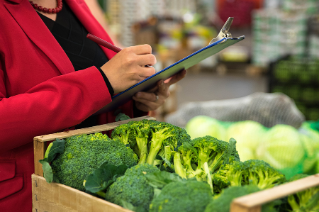 Food Safety Woman holds clipboard while standing next to broccoli at a grocery store