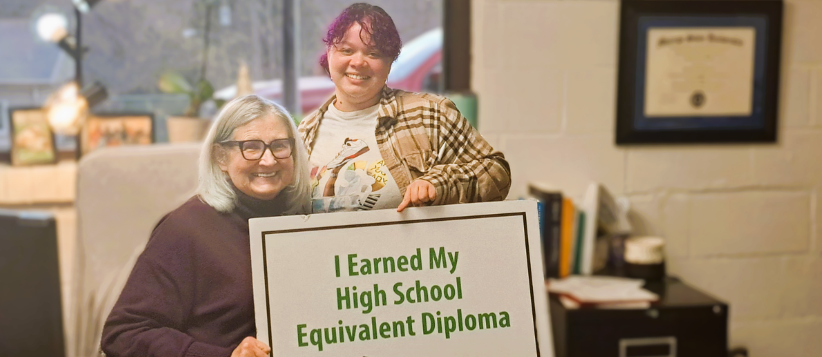 Two women smile while holding sign that says I Earned My High School Equivalent Diploma