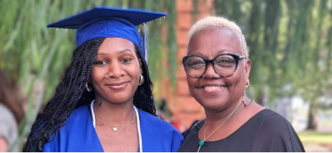 Woman wearing a mortarboard and graduation gown stands next to other woman