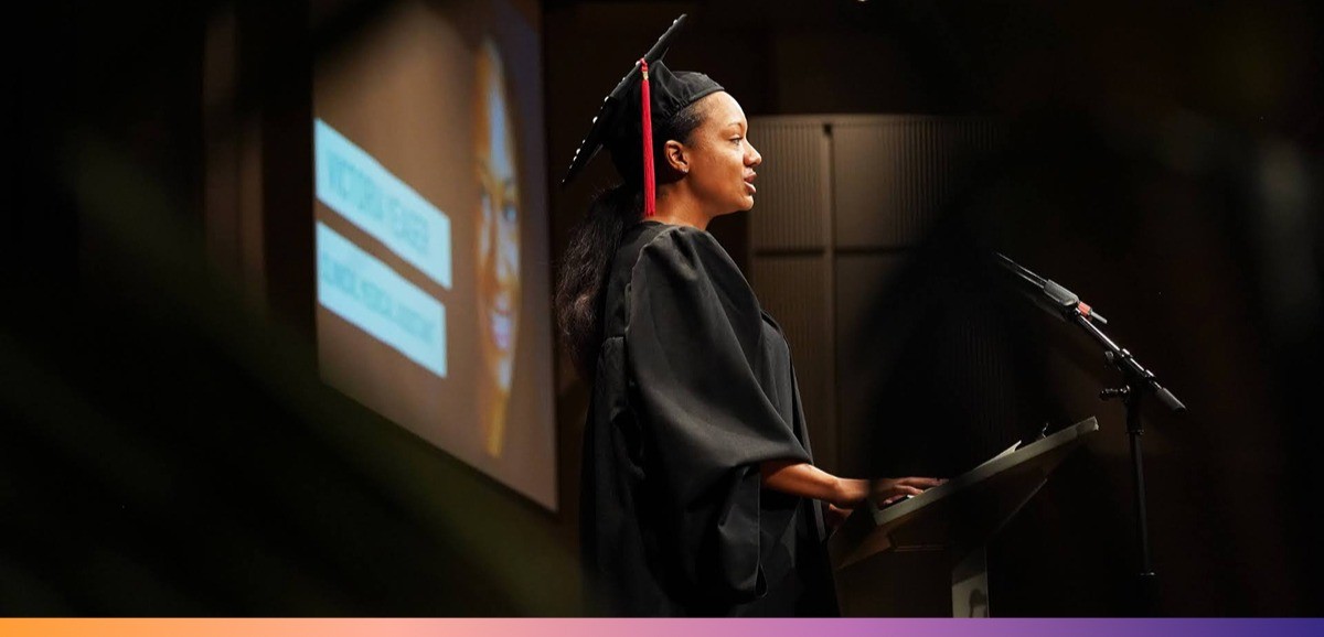UpRise Nashville A woman wearing a cap and gown speaks in front of a podium and microphone
