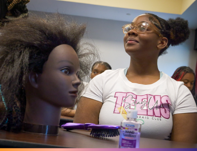 Youth Employment Program Girl smiles while sitting at a table that has a hairbrush and a mannequin head